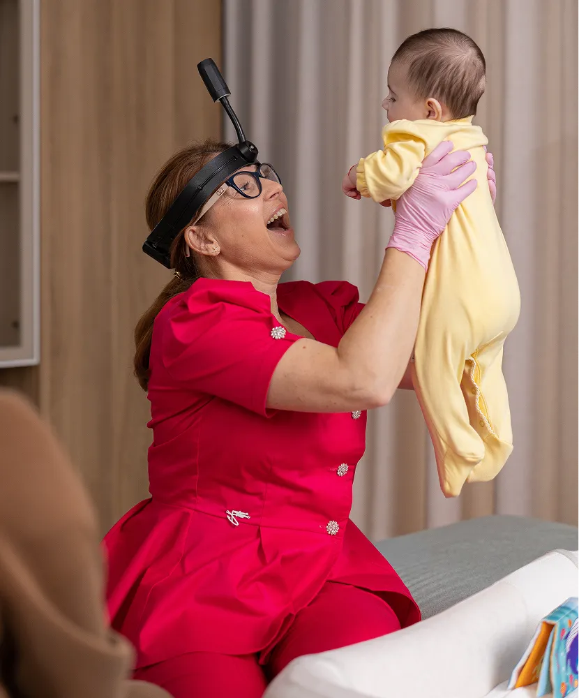 Dr. Cosmina Dușan jucându-se cu un bebeluș pentru acomodare și încredere înaintea evaluării orale